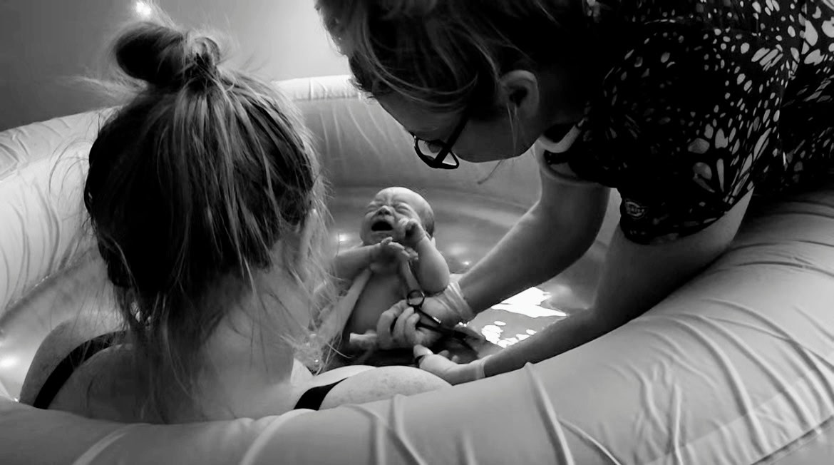 Midwife assisting during a water birth as a newborn is welcomed